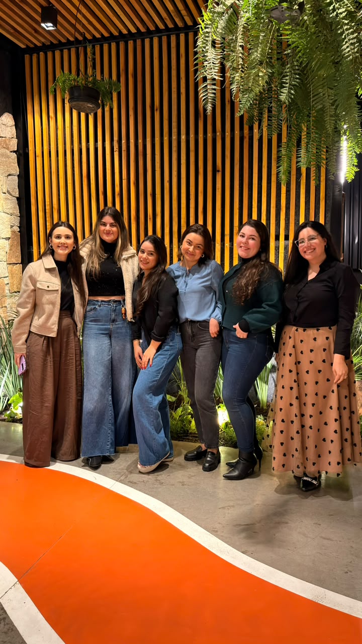 Grupo de amigas reunidas em frente a uma parede de madeira e plantas